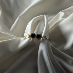 Gold ring with black gemstones on a white fabric background