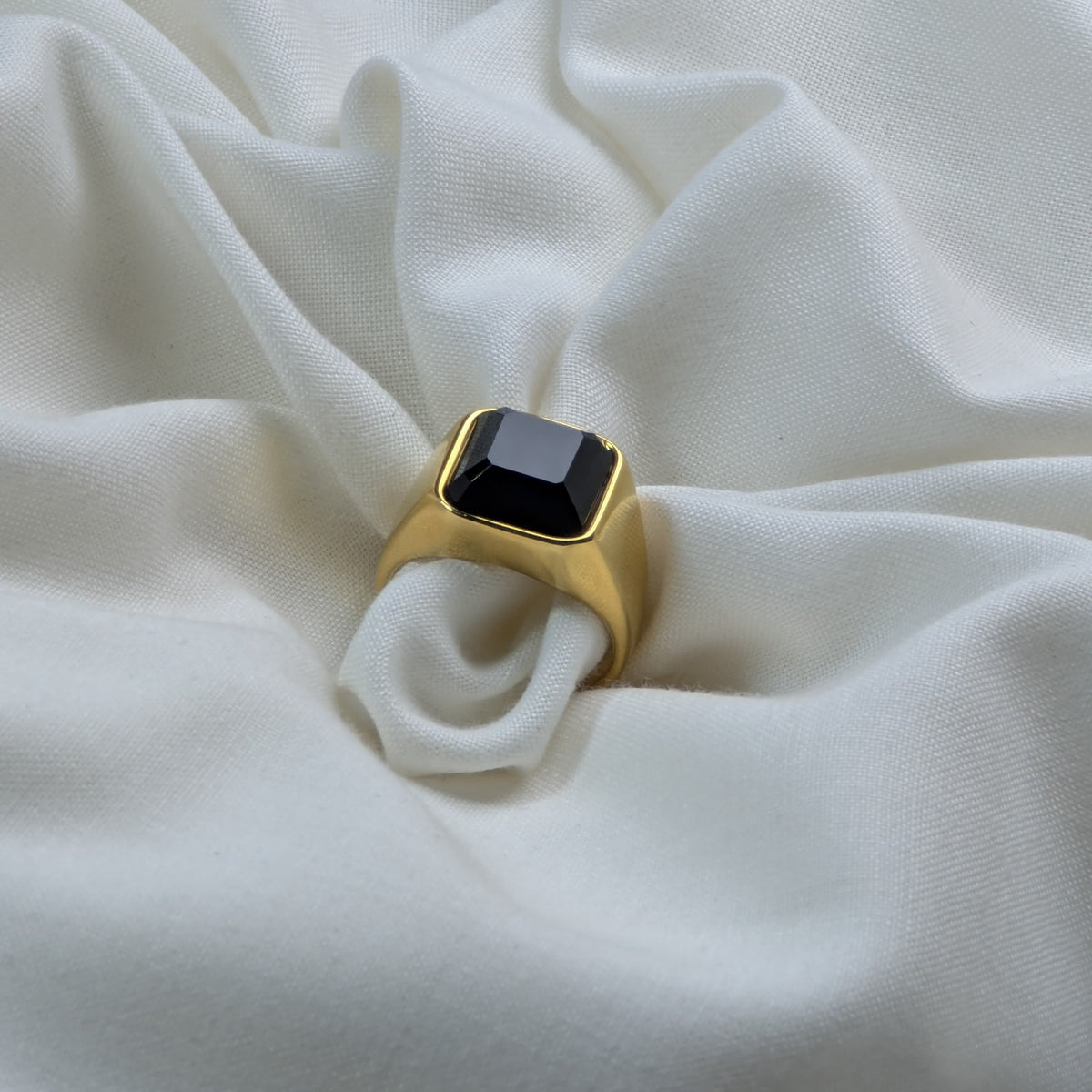 Gold ring with a black gemstone on a white fabric background