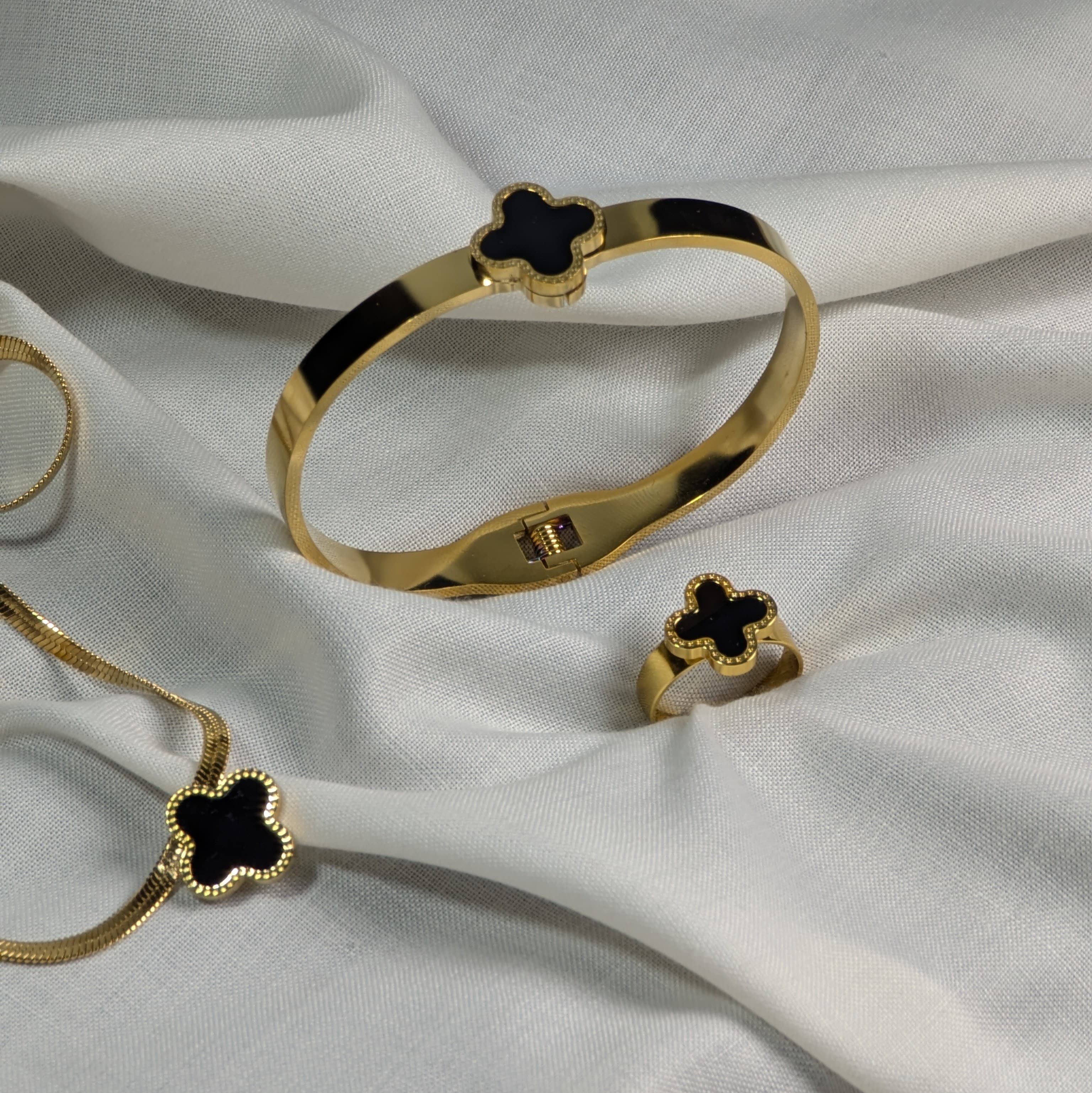 Gold bracelet and ring with black clover design on a white fabric background
