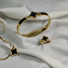 Gold bracelet and ring with black clover design on a white fabric background