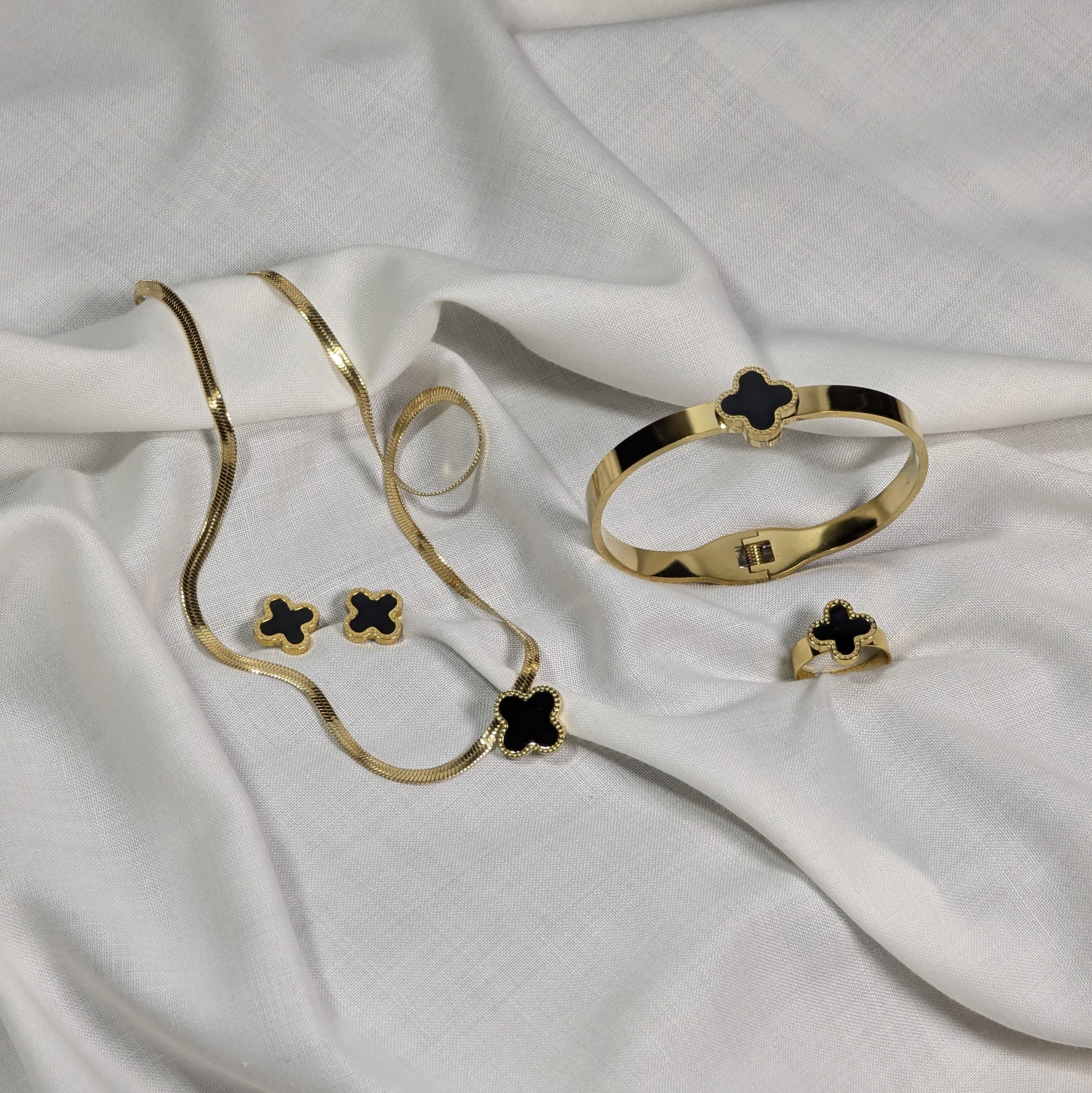 Gold jewelry set with black clover designs on a white fabric background