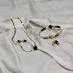 Gold jewelry set with black clover designs on a white fabric background
