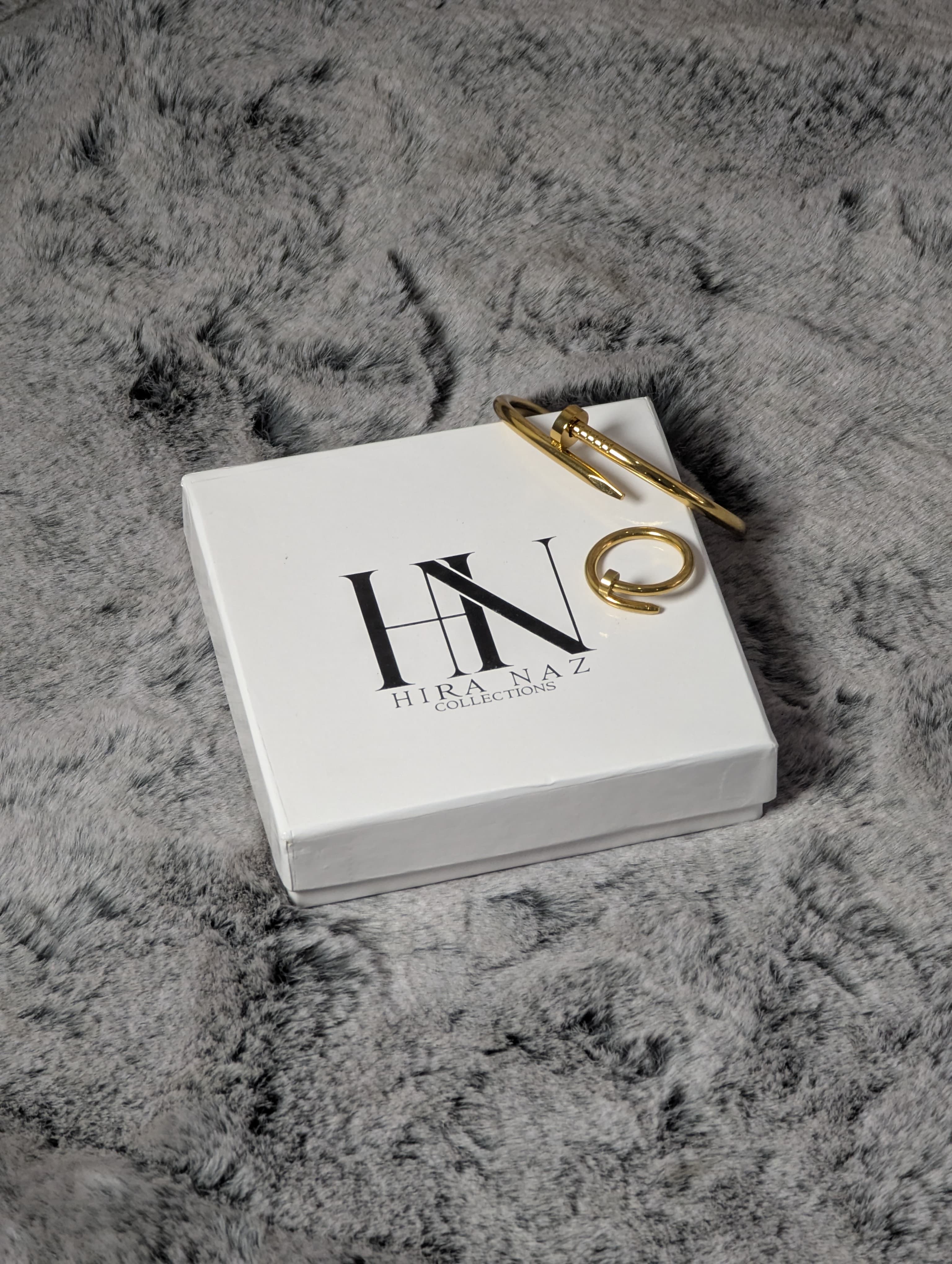 Gold ring on a white box with 'HN' branding on a textured gray surface