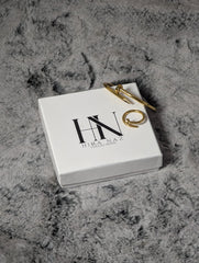 Gold ring on a white box with 'HN' branding on a textured gray surface