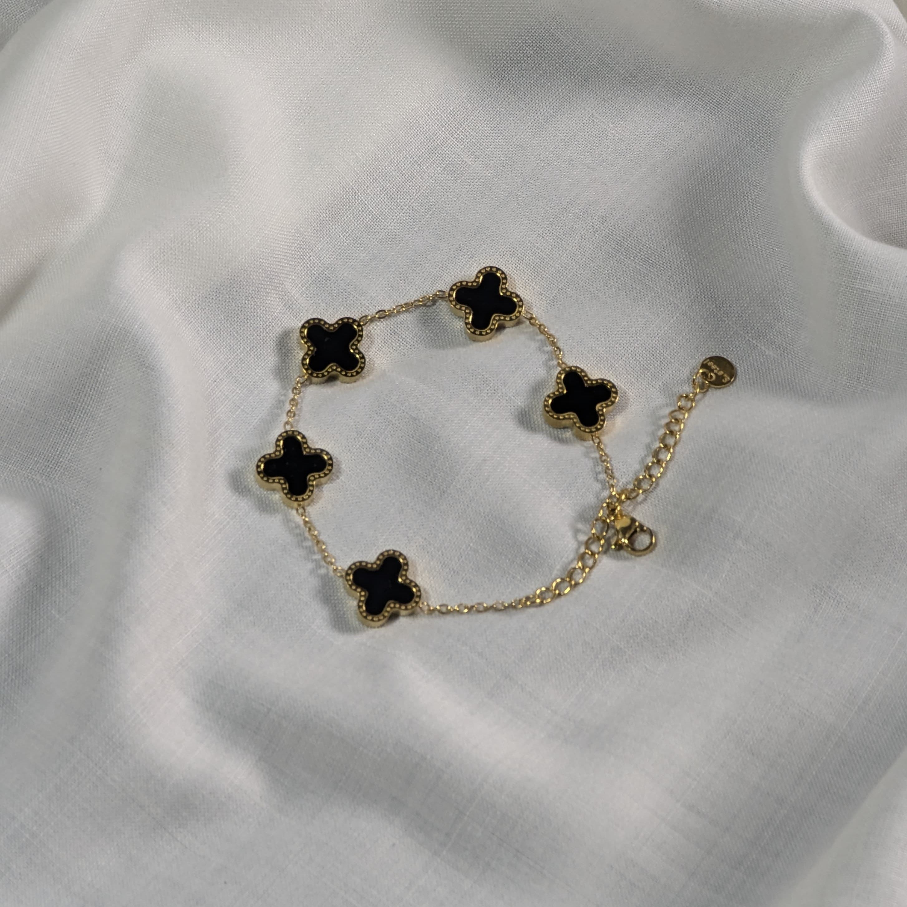 Gold bracelet with black clover-shaped charms on a white fabric background