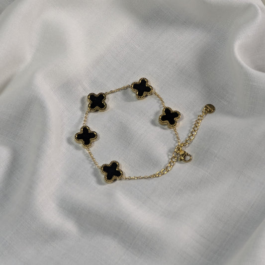Gold bracelet with black clover-shaped charms on a white fabric background