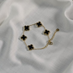 Gold bracelet with black clover-shaped charms on a white fabric background