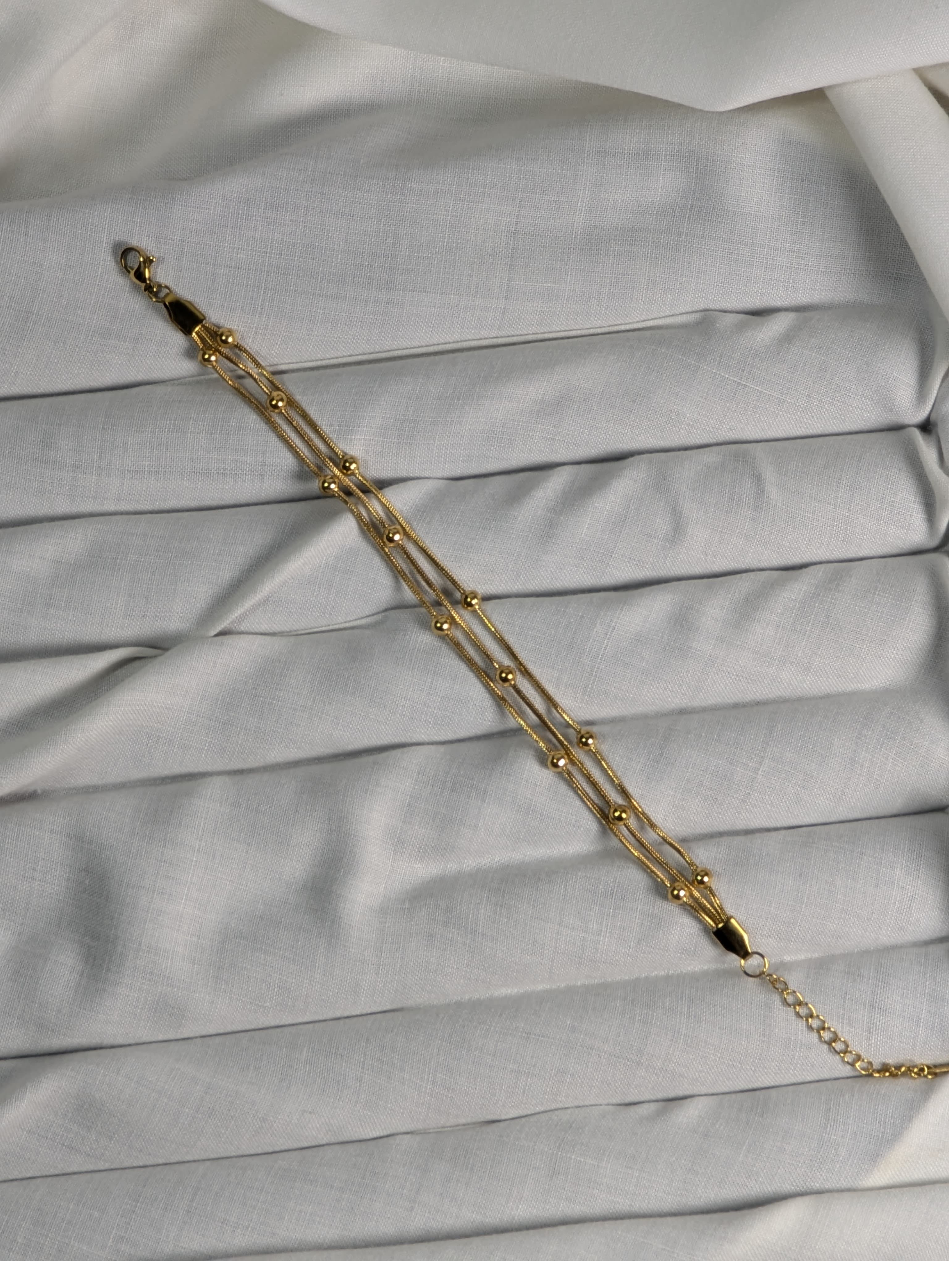 Gold chain bracelet on a light gray fabric background